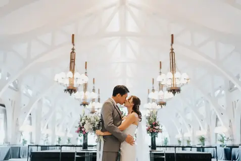 Newlyweds kissing in a bright hall with chandeliers