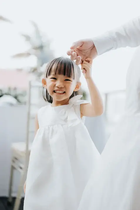 Smiling flower girl in white dress holding hands