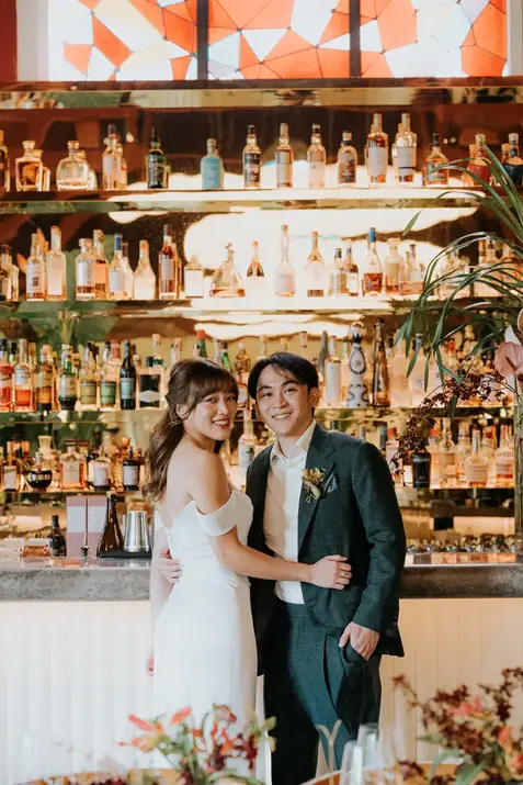 Bride and groom posing in front of a bar at Claudine.