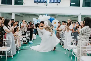 Groom dipping bride for a kiss during wedding march-in at a school hall wedding in Singapore.