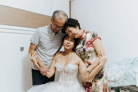 Bride in white gown embraced by her parents at wedding