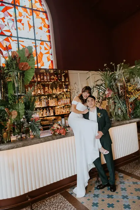 Bride Claudine sitting on a bar with her groom.