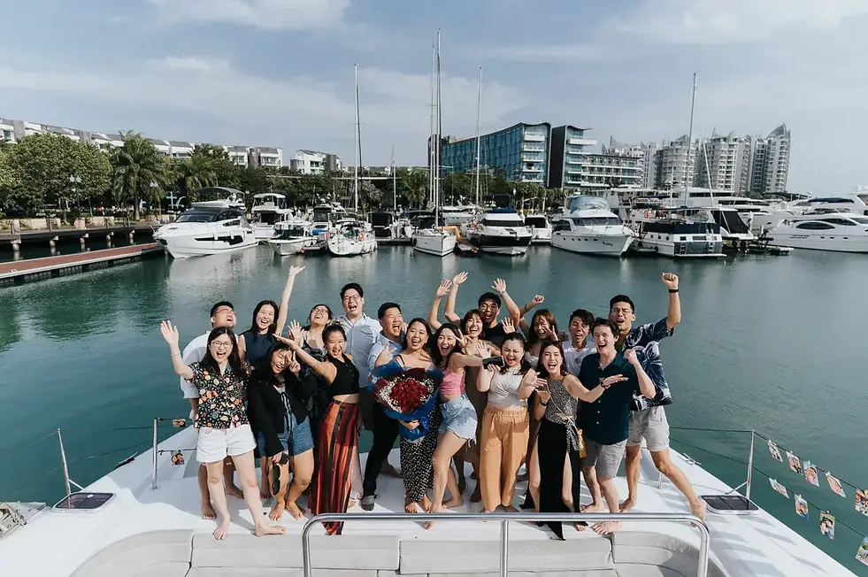 Fun yacht proposal at sea with panoramic views of Singapore's coastline of the couple celebrating with family and friends.