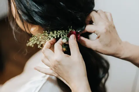 Stylist placing floral hairpiece into bride's dark hair