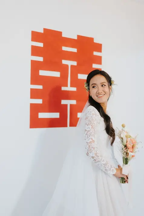 Bride in white lace holding bouquet by Double Happiness symbol