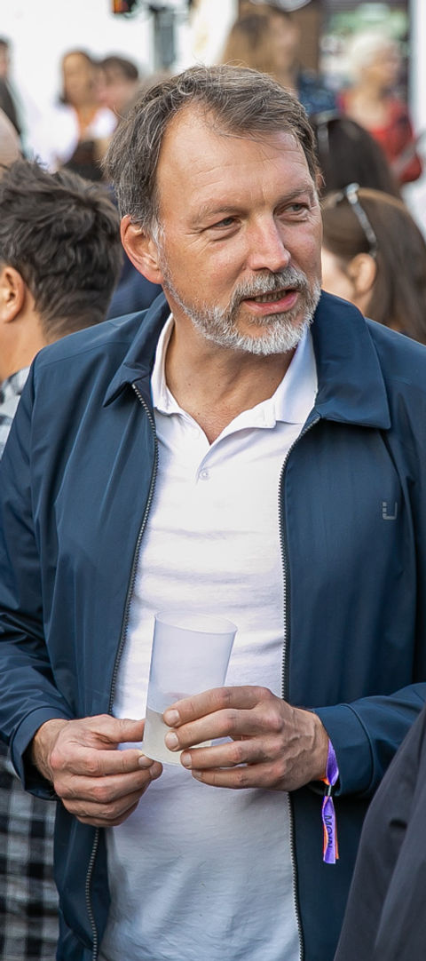 Ein Mann in einer blauen Jacke hält einen Becher, während er mit zwei Personen auf einem Event in Hamburg spricht.