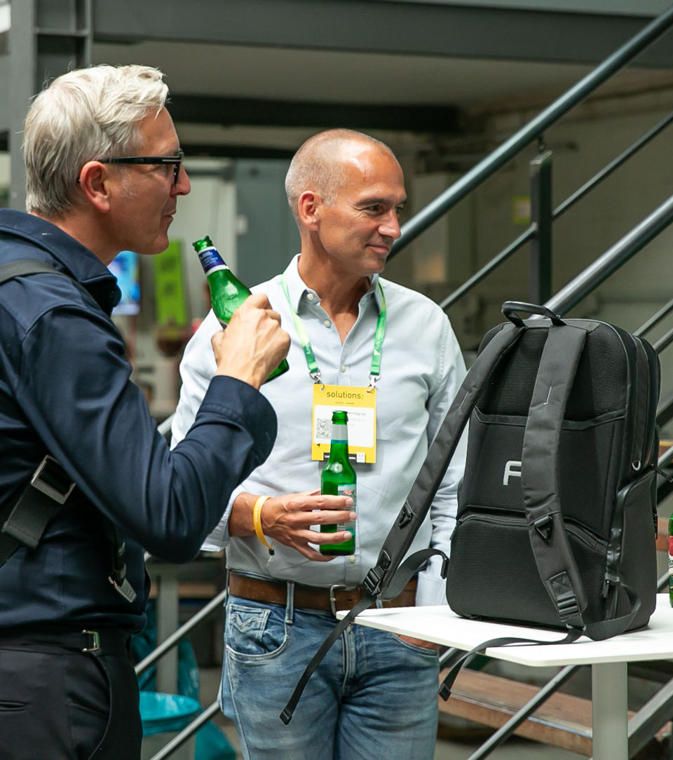Zwei Männer, die Bier trinken, unterhalten sich mit einer Frau an einem Stehtisch auf einem Event in Hamburg.