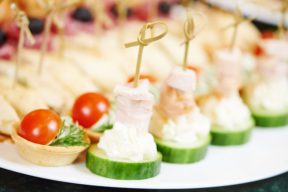 Colorful appetizer canapés on a white plate, with cucumber, cream, ham, cherry tomatoes, and tartlets on skewers.