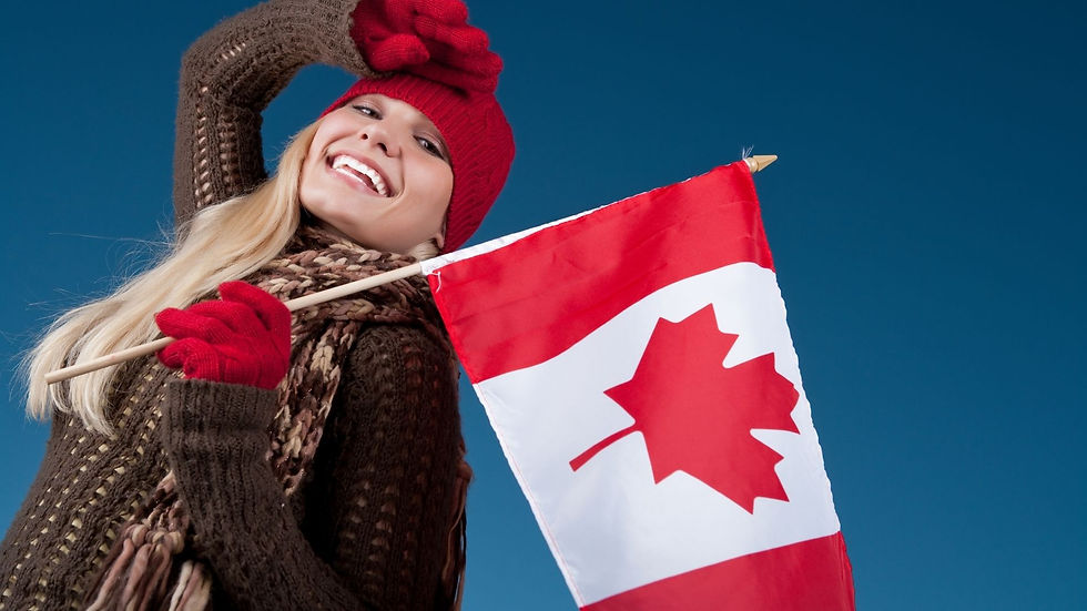 Smiling woman in red hat and gloves holds a Canadian flag against a clear blue sky.