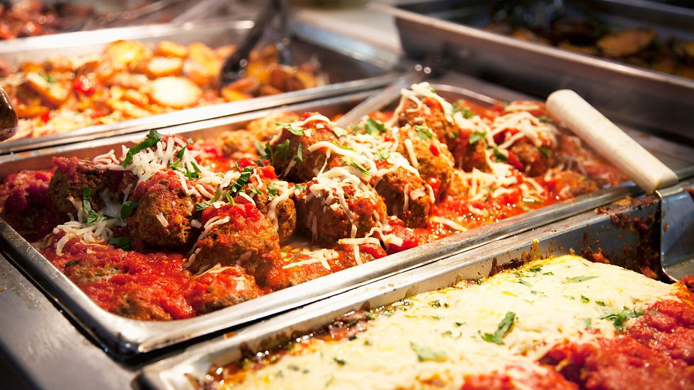 Buffet trays of meatballs in red sauce topped with melted cheese and herbs, under warm restaurant lighting.