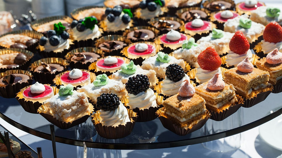 Assorted mini pastries and fruit-topped desserts on a glass tray, colorful and neatly arranged in bright daylight.