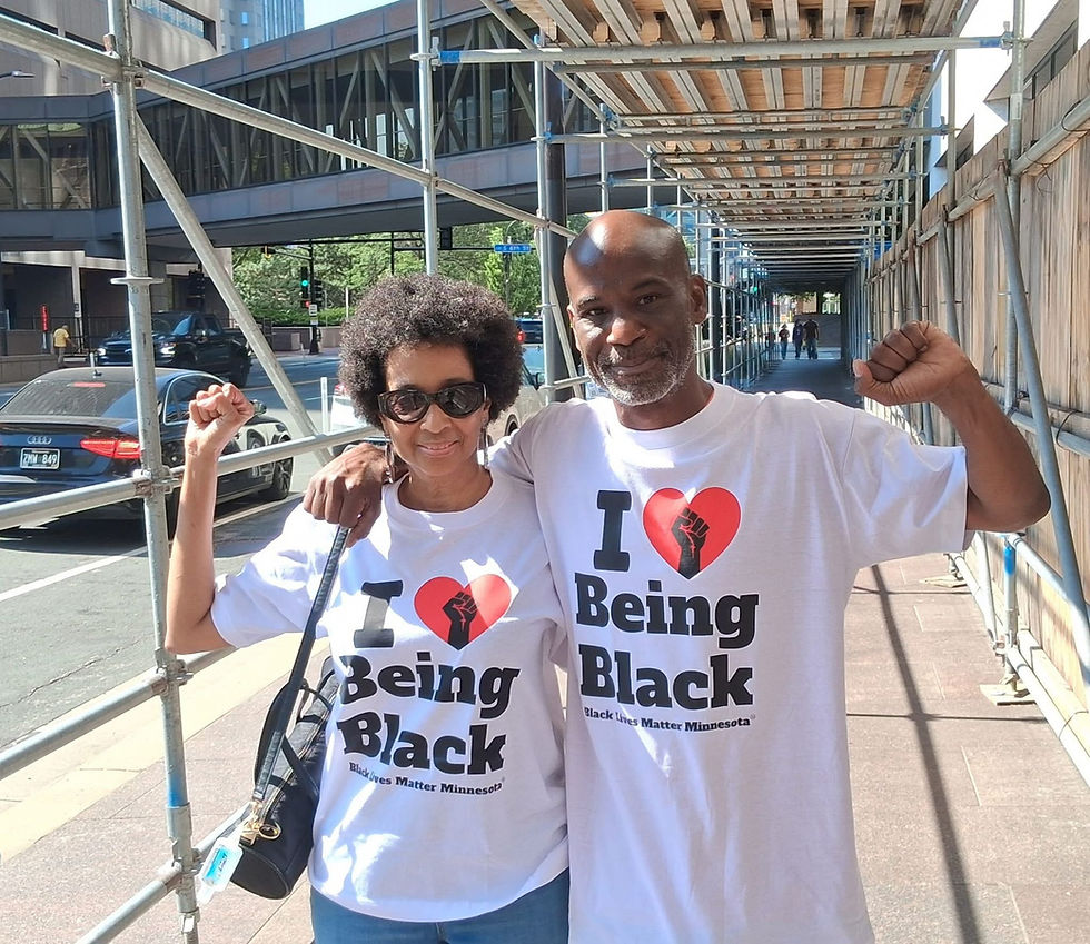 Two people wearing 'I love being black' t-shirts standing arm and arm and smiling.
