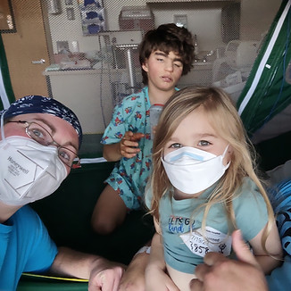Katelyn and her family posing for a picture in a hospital room, where they are each wearing masks while visiting their son.