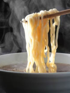 Steaming noodles held by chopsticks above a bowl of soup, close up.