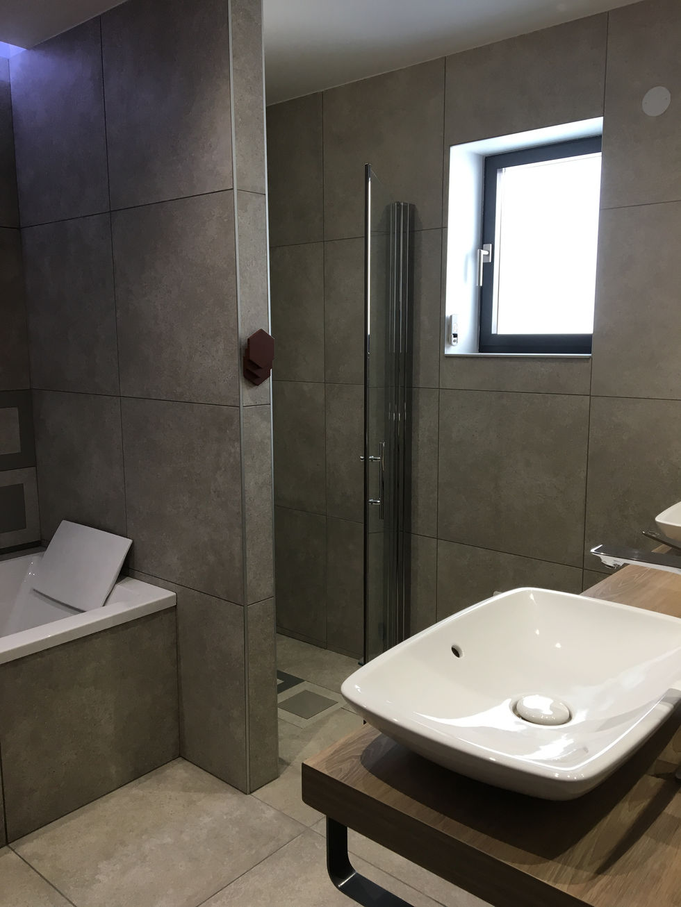 Salle de bain moderne avec carreaux à motifs, double vaque, meuble imitation chêne et baignoire avec mitigeur sur pied.