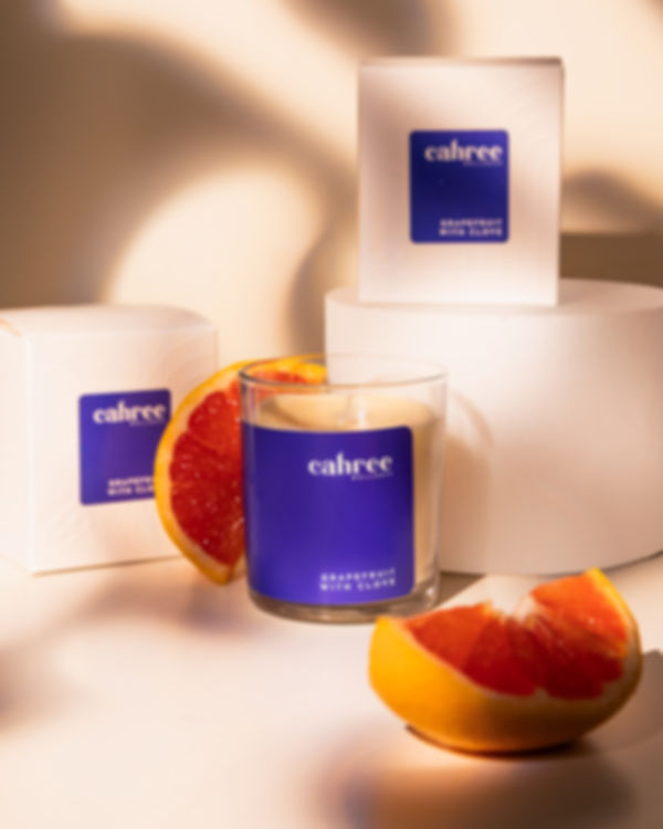 Cahree Grapefruit & Clove luxury soy candle in violet glass, styled with grapefruit slices and white gift boxes under warm li