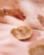 Golden ceramic petal-shaped trinket tray holding rings and jewellery on a soft pink surface in a minimal setting.