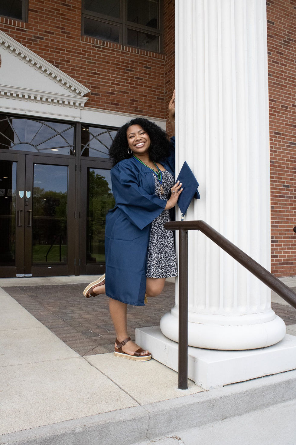 A picture of Caitlin standing and smiling on the chapel steps in her cap and gown