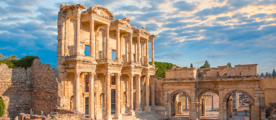 Ancient ruins with tall, intricate stone columns and arches under a partly cloudy blue sky, evoking a sense of historical grandeur.