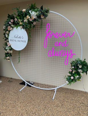 Forever and always neon sign with white circular mesh stand and spring flower garland for bridal shower