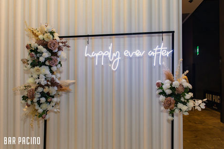 Black frame stand with happily ever after neon sign and mocha and white rose flower garland at Bar Pacino