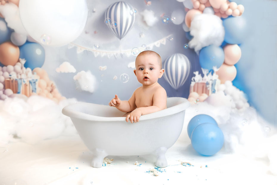 1 year old boy sits in bath tub against hot air balloon theme backdrop
