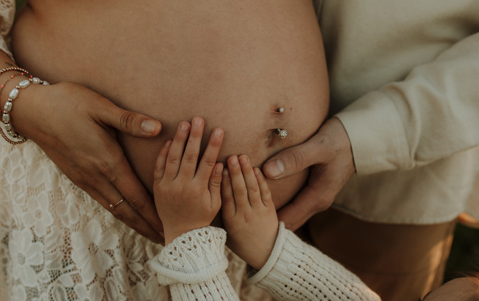 mom, daughter, and dad put hands on pregnant belly