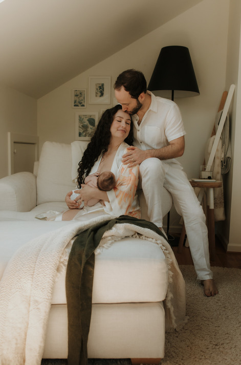 a husband kisses his wife on the forehead while she holds her newborn baby
