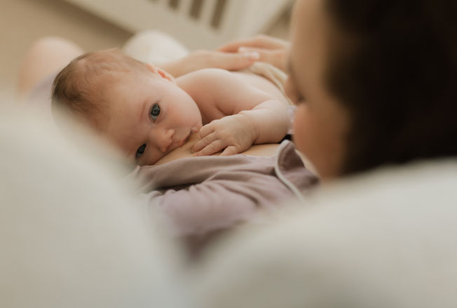 a baby breastfeeds while looking up at the camera