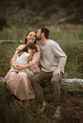 mom and dad cuddle daughter at the beach during a photo session