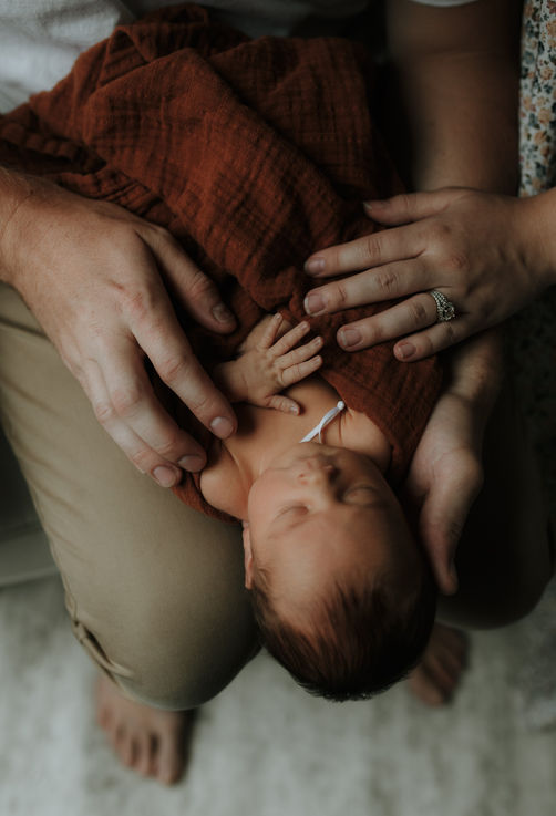a newborn lays in the lap of her father