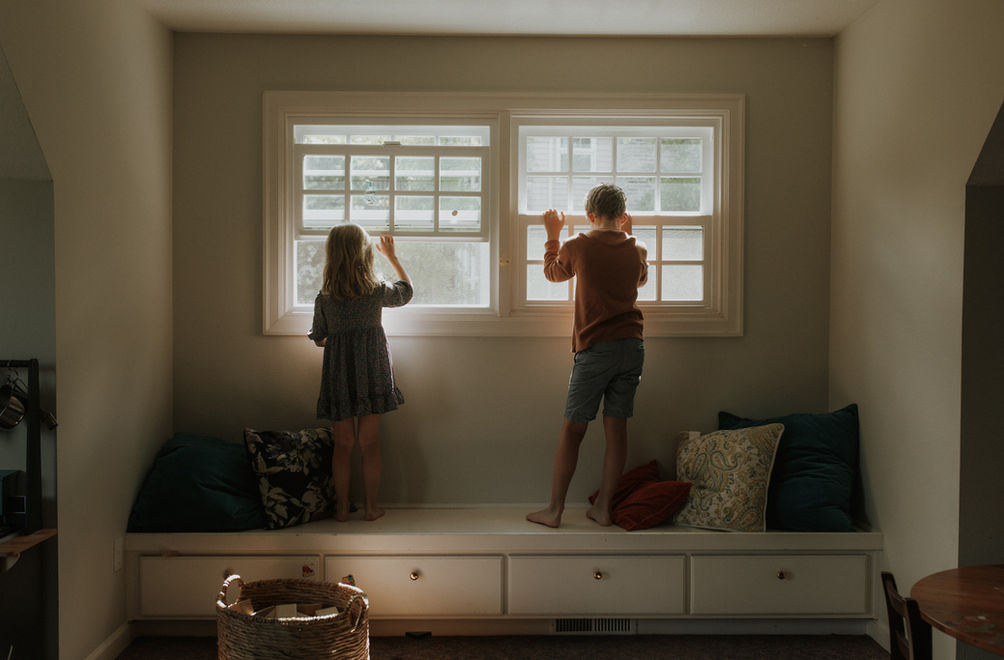 a son and daughter look out their home window in the sunlight