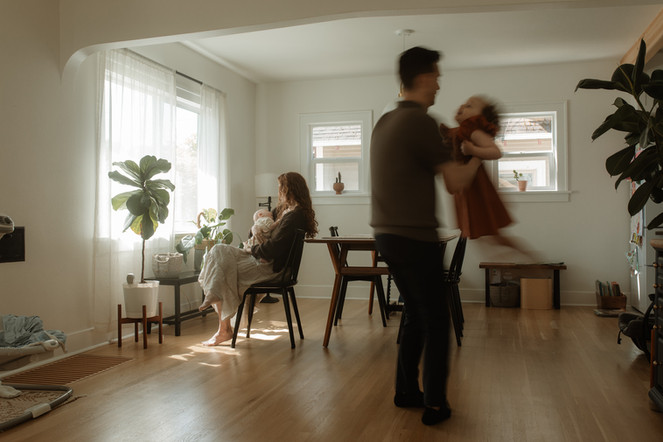 dad and daughter dance while mother holds newborn baby in background