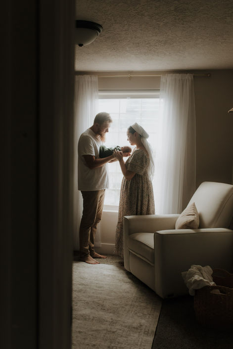 a family holds their newborn baby in front of a window in their Woodburn oregon home