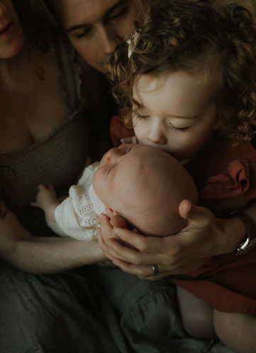 older sister kisses newborn on forehead during a photography session