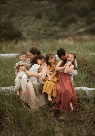 family sits on beach log and laughs during a photo session