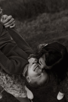sister kisses brother and he's laughing being held upside down by his mother during motherhood session in portland, oregon.