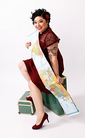 Tia in a maroon dress, holding a map and sitting on top of suitcases