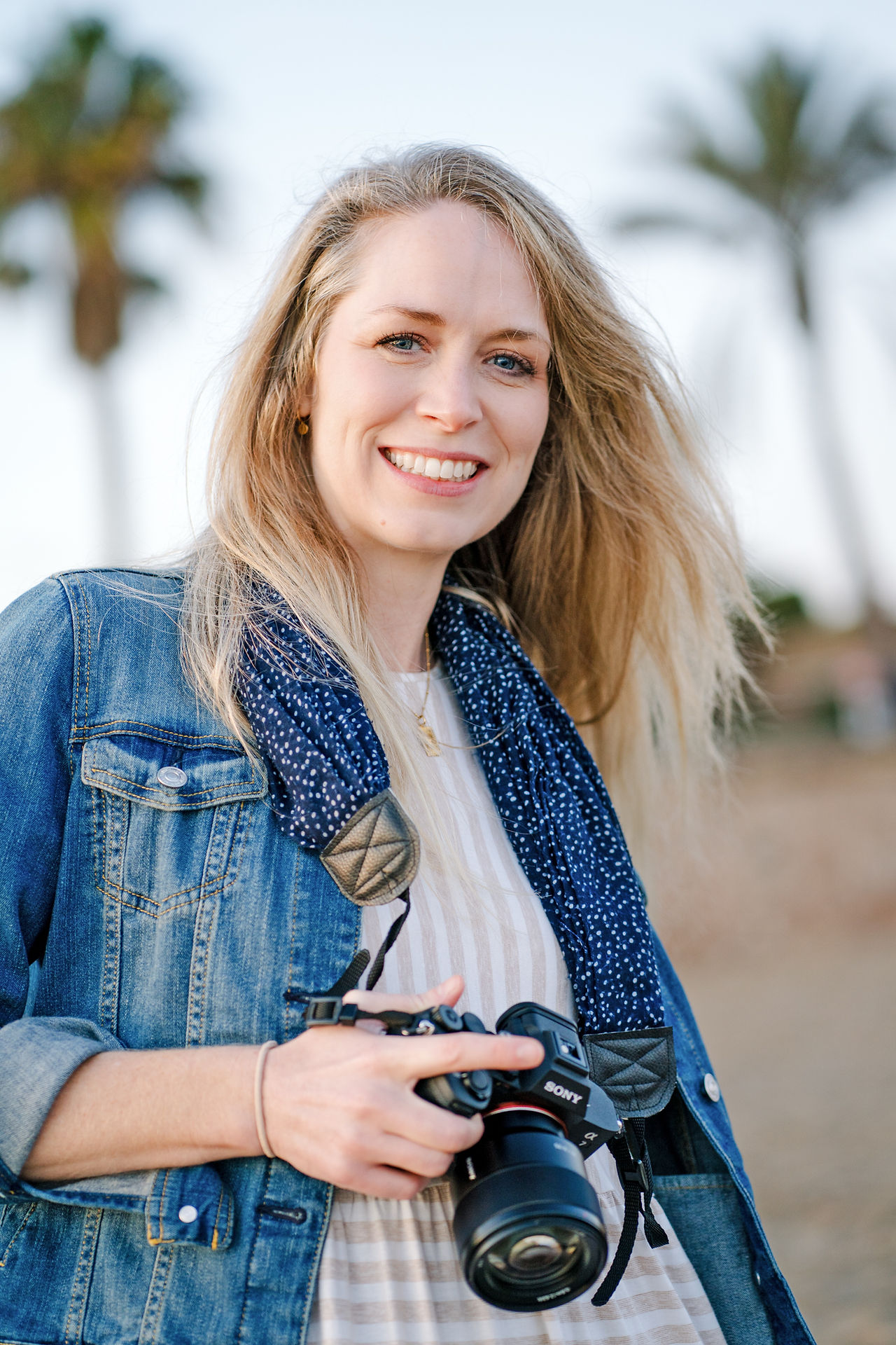 Woman with camera smiling at photographer on the beach