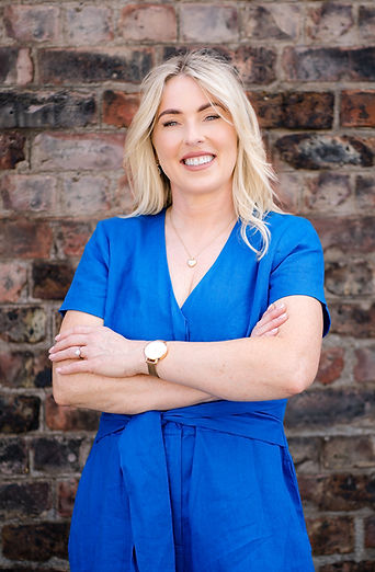 Woman standing by brick wall, arms crossed with a blue dress on