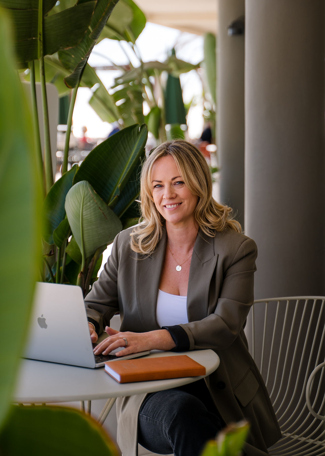 Business woman smiling at camera whilst working on laptop surrounded by plants