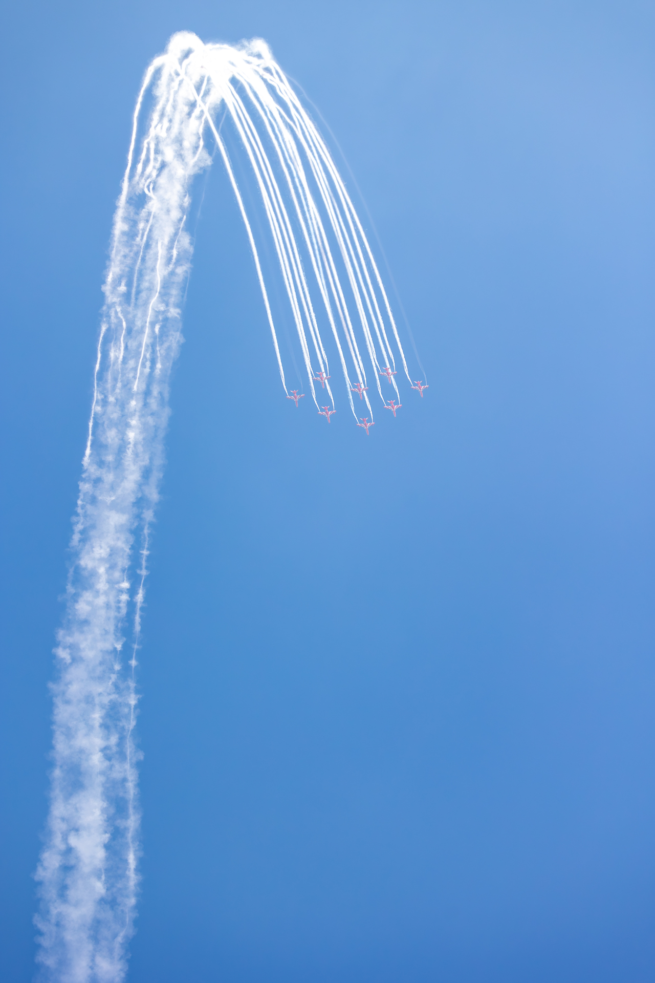 Aerobatic aircraft leaving curved smoke trails in a blue sky during the Bangalore airshow