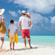 Family of 4 on the beach walking towards the clear blue water