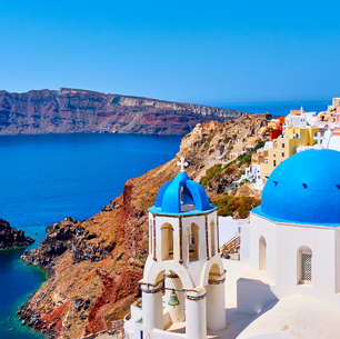 View of Santorini with white buildings and blue roofs overlooking the ocean with a mountain in the background