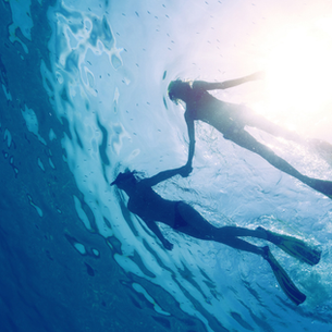 Two snorkelers silhouetted underwater with sunlight shining through the ocean surface