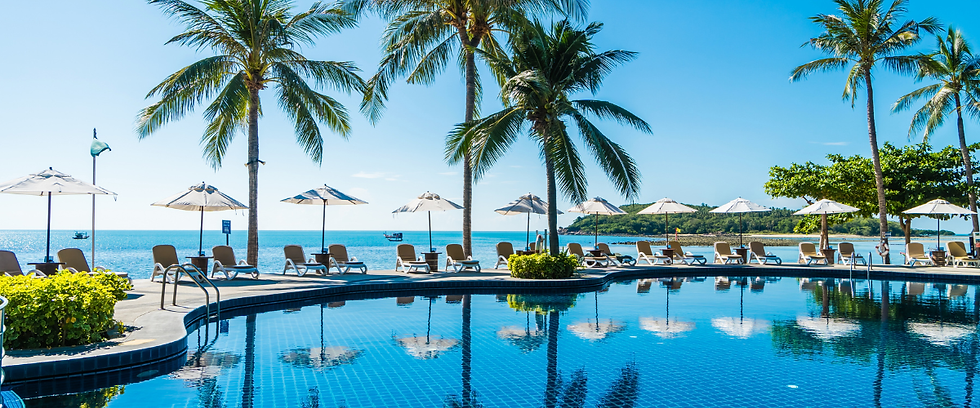 Luxury beachfront resort with an infinity pool, palm trees, sun loungers, and ocean views on a sunny tropical day.