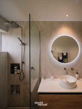 Modern bathroom in high performance home NZ with round mirror, timber vanity, and energy efficient design