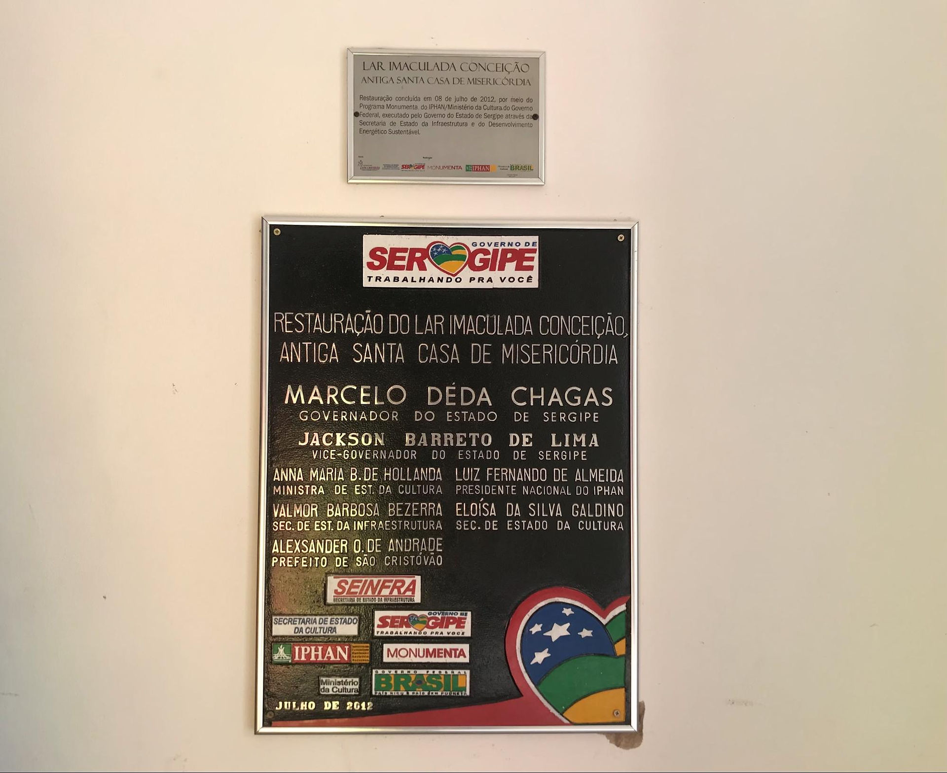 #PraCegoVer: Placa de restauração do Lar Imaculada Conceição presa à parede do local.