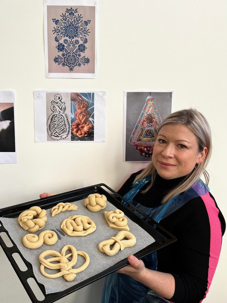 A woman holding a tray of dough woven into a variety of patterns