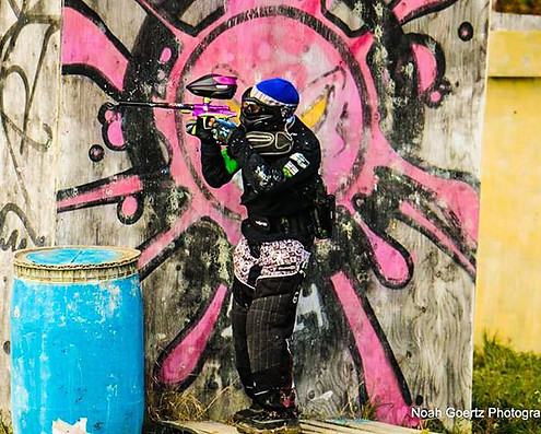 A man in full paintball gear aiming a paintball gun, standing in front of a grafitti wall at DMZ Canada Paintball and Airsoft, Niagara's best paintball and airsoft field, Niagara Falls Ontario